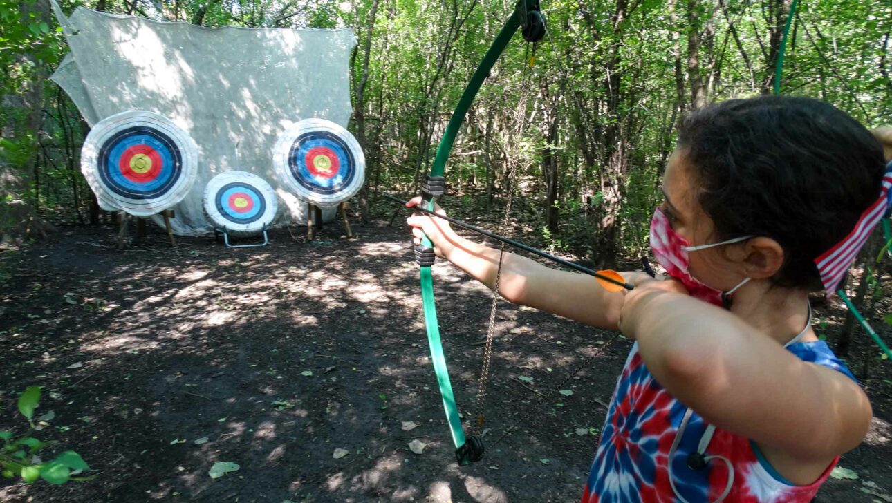 A camper aiming a bow and arrow at targets.