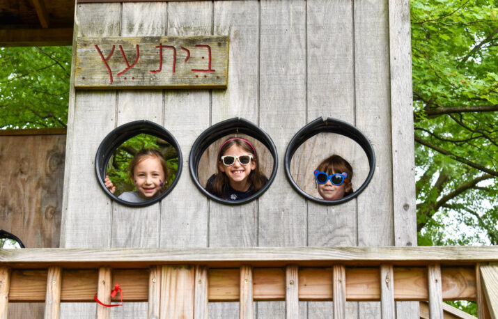 Girls in a tree house looking outside a window.