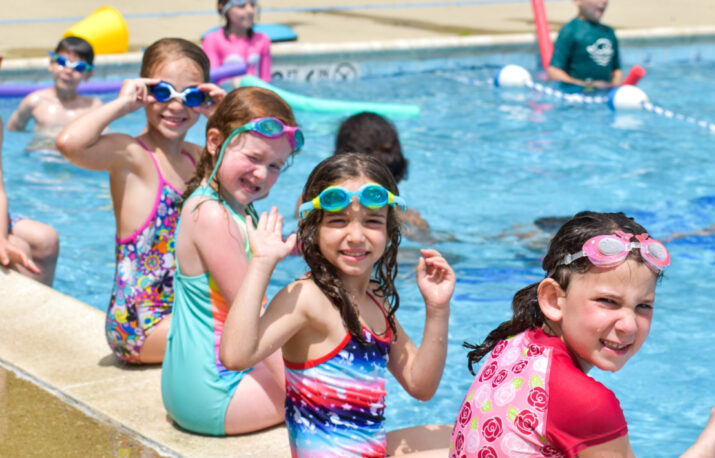 A group of girls sitting on the side of the pool.