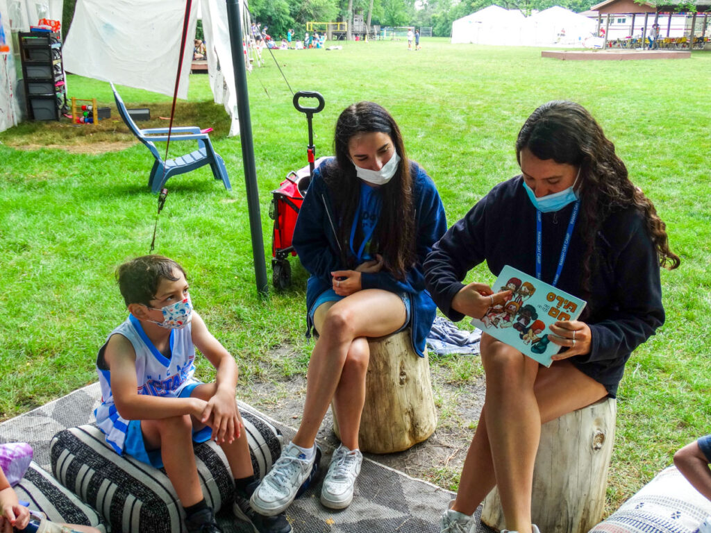 Two girl counselors sitting and read with a camper.