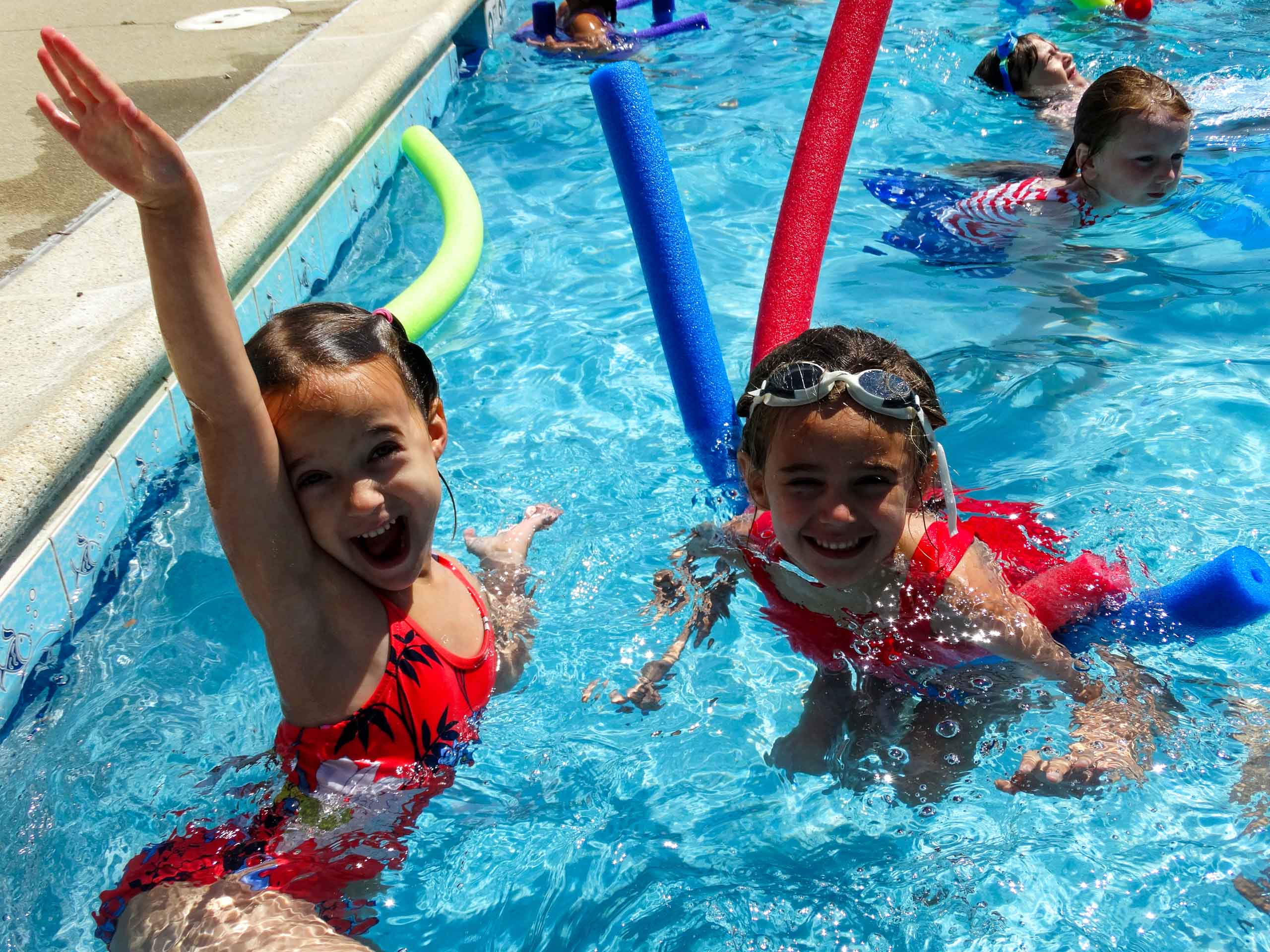 Two young campers swimming with pool noodles.