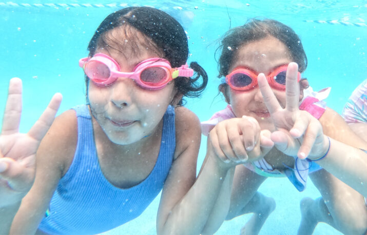 Two girls underwater wearing goggles.