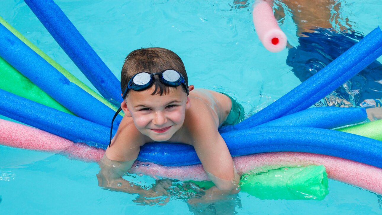 A boy in a pool laying on many pool noodles.